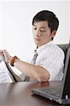 Young businessman holding newspaper and looking at wrist watch