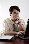 Young businessman sitting in an office talking on the telephone and using laptop
