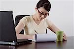 Young businesswoman sitting at desk and writing on paper