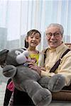 Granddaughter and grandfather holding teddy bear, smiling, portrait