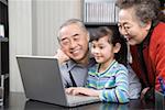 Girl with grandmother and grandfather using laptop, smiling