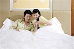 Young couple lying on bed and reading text message, smiling