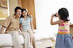 Daughter photographing mother and father sitting on bed