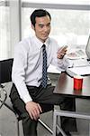 Young businessman holding mobile phone in an office, smiling