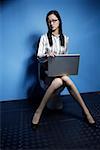 Young woman using laptop on commode, portrait