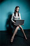 Young woman sitting on commode and using laptop, portrait