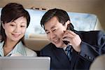 Businessman and woman in car using mobile phone and laptop