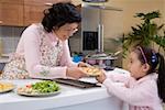 Grandmother handing dish to granddaughter in kitchen