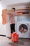 Young woman holding shirt while girl sitting in washing machine and smiling