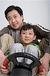 Father and son holding steering wheel, smiling