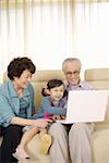 Girl sitting with grandfather and grandmother looking at laptop