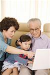 Girl sitting with grandfather and grandmother looking at laptop