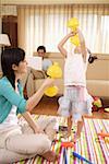 Young woman playing with daughter while man sitting on sofa using laptop