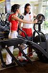 Young man instructing young woman on exercise machine