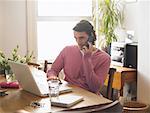 Portrait of Man Sitting at Table using Laptop Computer and Cell Phone