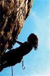 Silhouette of a female rock climber holding onto a rock with the help of a rope