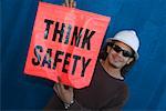 Close-up of a male construction worker smiling and holding a warning sign