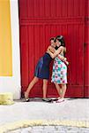 Two young women hugging each other in front of a gate and smiling