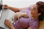 Young woman using a laptop and a puppy lying on her