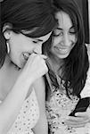 Close-up of two young women text messaging and smiling