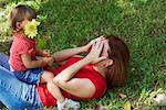 Junge Frau am Gras liegen und die ihr Gesicht mit ihren Händen und ihrer Tochter sitzt auf dem Bauch