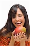 Close-up of a young woman holding a mango and laughing