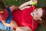 Young woman lying on grass with her daughter sitting on her stomach