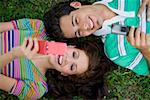 High angle view of a young couple lying in a park and holding mobile phones