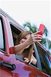 Young woman sitting in a car and taking a picture with a mobile phone