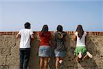 Vue arrière de trois jeunes femmes et un jeune homme regardant par dessus un mur de Pierre, Morro Castle, le vieux San Juan, San Juan, Puerto Rico
