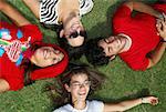 Three young women with a young man lying on grass and smiling