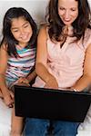 Vue grand angle d'une femme adulte milieu à l'aide d'un ordinateur portable avec sa fille assise à côté d'elle et souriant