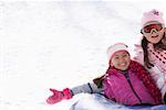 Mid adult woman with her daughter sliding down snowy slope on an inner tube