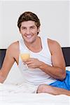 Portrait of a mid adult man sitting on the bed and holding a glass of orange juice