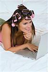 Jeune femme portant des bigoudis et à l'aide d'un ordinateur portable sur le lit