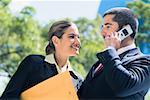 Businessman talking on a mobile phone with a businesswoman smiling beside him