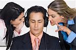 Close-up of a businessman listening to music while two businesswomen bothering him