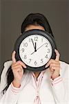 Gros plan d'une femme d'affaires cachant son visage avec une horloge