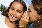 Close-up of a mid adult woman whispering into her daughter's ear