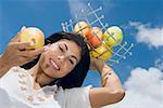 Vue d'angle faible d'une femme adulte mid tenant un plateau de fruits sur sa tête et montrant une pomme
