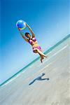 Vue d'angle faible d'une femme adulte milieu jouant avec un ballon de plage sur la plage