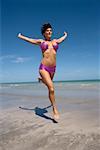 Mid adult woman running on the beach with her arms outstretched