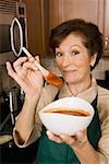 Porträt einer leitenden Frau hält eine Schüssel Tomatensuppe und einen Holzlöffel in der Küche