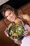 Close-up of a young woman mixing salad in a colander