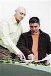 Two architects standing near a model and discussing a blueprint