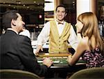 Rear view of a mature man and a young woman sitting at a gambling table with a casino worker smiling in front of them