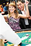 Young woman cheering at a gambling table with a mature man standing beside her in a casino