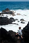 Vue arrière d'un garçon debout sur une îles de falaise, la plage de Kehen, Big Island, Hawaii, USA
