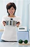 Woman in kitchen, holding crocking pot towards camera