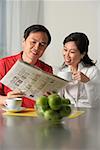 Mature couple looking at newspaper and having coffee
